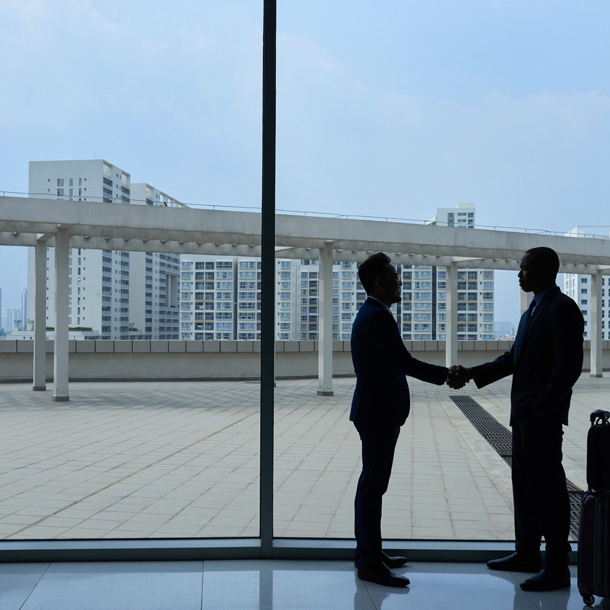 Business people standing against big airport window and shaking hands